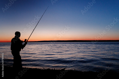 Silhouette of a fisherman with a fishing rod at a beautiful sunset. Against mountains