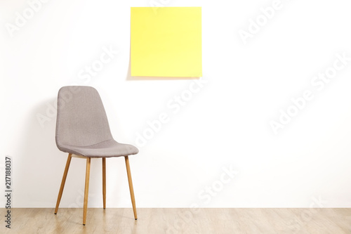 Fototapeta Naklejka Na Ścianę i Meble -  Single empty loft style gray chair on wooden floor, blank ad poster and white wall background, yellow sticker with copy space for your text. Interview invitation for vacant position concept. Close up.