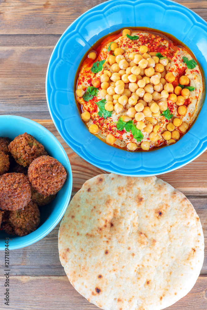 Falafel balls in a dish, pita bread and hummus, chickpea, tahini with olive oil, pepper, spices in a plate on wood background. Traditional Middle Eastern healthy vegan food.Flat lay, top view. Falafel balls in a dish, pita bread and hummus, chickpea, tahini with olive oil, pepper, spices in a plate on wood background. Traditional Middle Eastern healthy vegan food.Flat lay, top view.