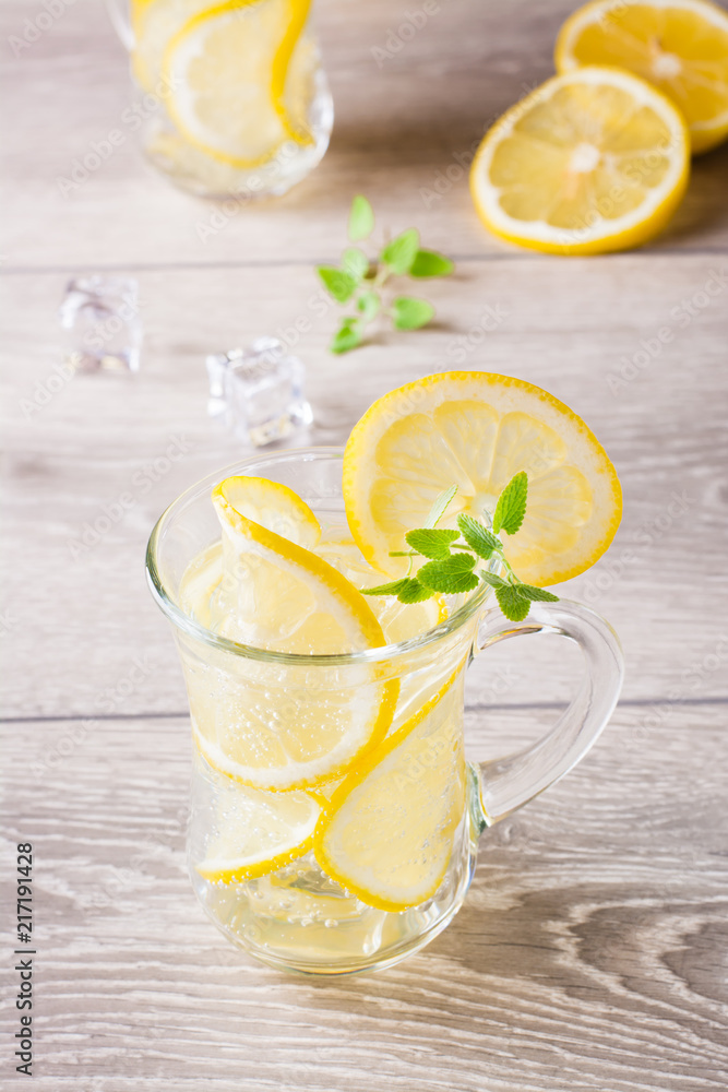 Refreshing cold mineral water with lemon, mint and ice cubes in glasses on a wooden table Refreshing cold mineral water with lemon, mint and ice cubes in glasses on a wooden table