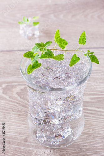 Cold mineral water with ice cubes and mint leaves in a transparent glass on a wooden table