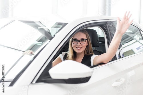 Business woman in glasses waving sitting in the cabin of a white car