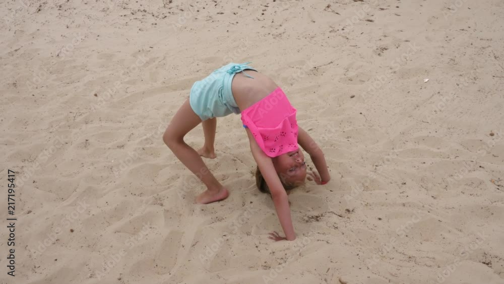 Young acrobatic girl doing gymnastic bridge and somersaults on sand Young acrobatic girl doing gymnastic bridge and somersaults on sand