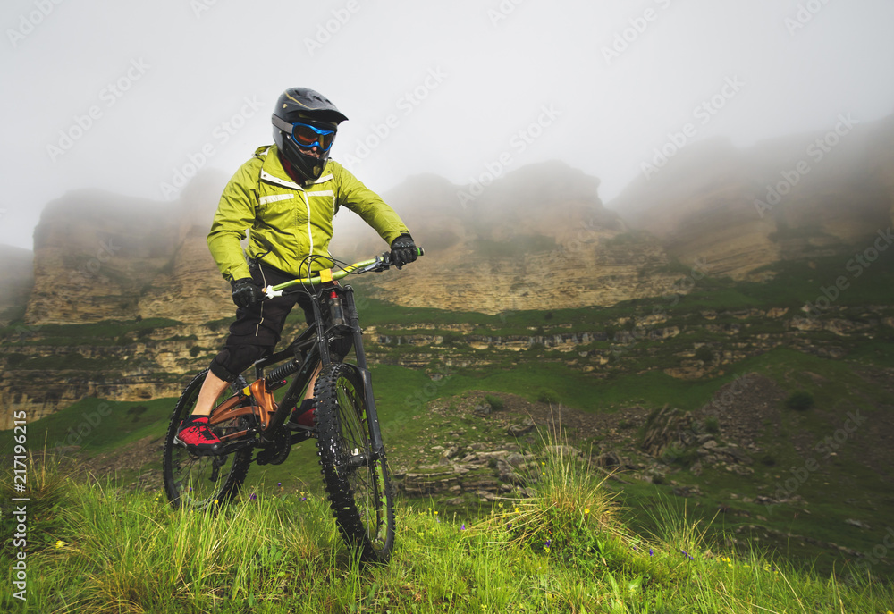 A man in a mountain helmet riding a mountain bike rides around the beautiful nature in cloudy weather. downhill