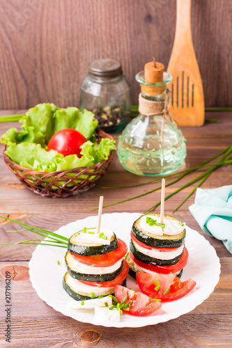 Original appetizer from fried zucchini, fresh tomatoes and feta cheese on a wooden skewer on a white plate