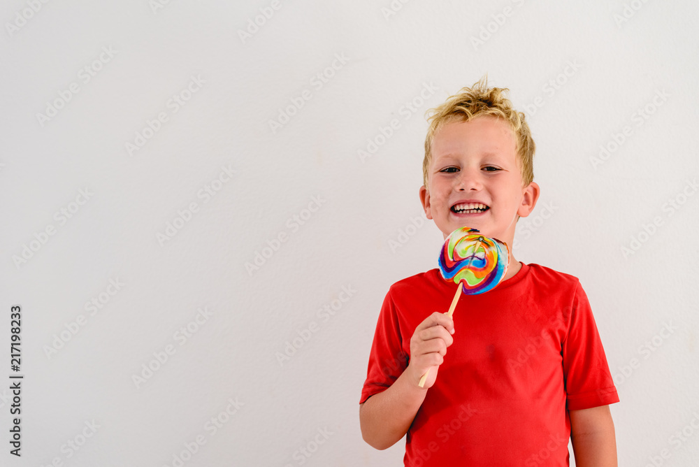 Boy with red shirt on white background eating a lollipop colorful fun and laughing. Boy with red shirt on white background eating a lollipop colorful fun and laughing.
