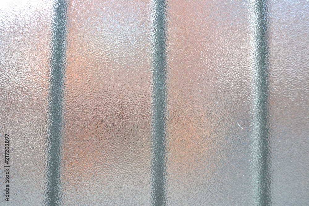 Closeup photograph of textured glass. Gray, blurry beams are visible in the background.