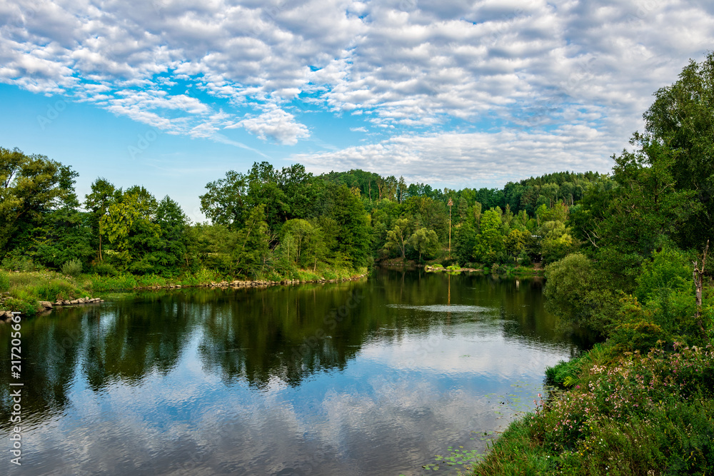 River with reflection of the clouds in the water and trees behind in the bavarian forest