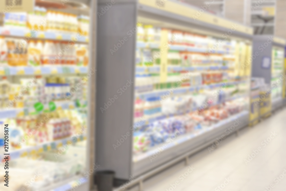 Blurred photo. Trade Hall of a large shopping center. Straight rows of shelves with bright colored goods.