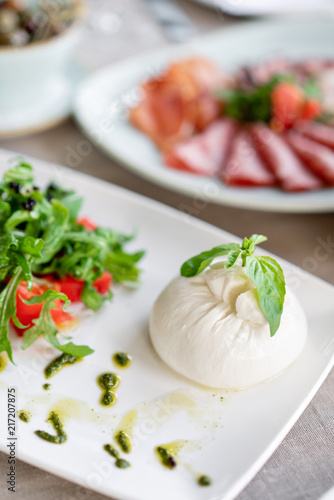 Italian Caprese salad. burrata cheese, tomatoes and basil herb leaves. Balsamic vinegar arranged on white plate