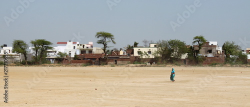 Elder woman walking in front of a desert village