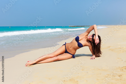 Sexy beautiful tanned woman relaxing and sunbathing in bikini on sea background and palm. Panoramic view from Jumeirah beach Dubai, UAE. Famous tourist destination.