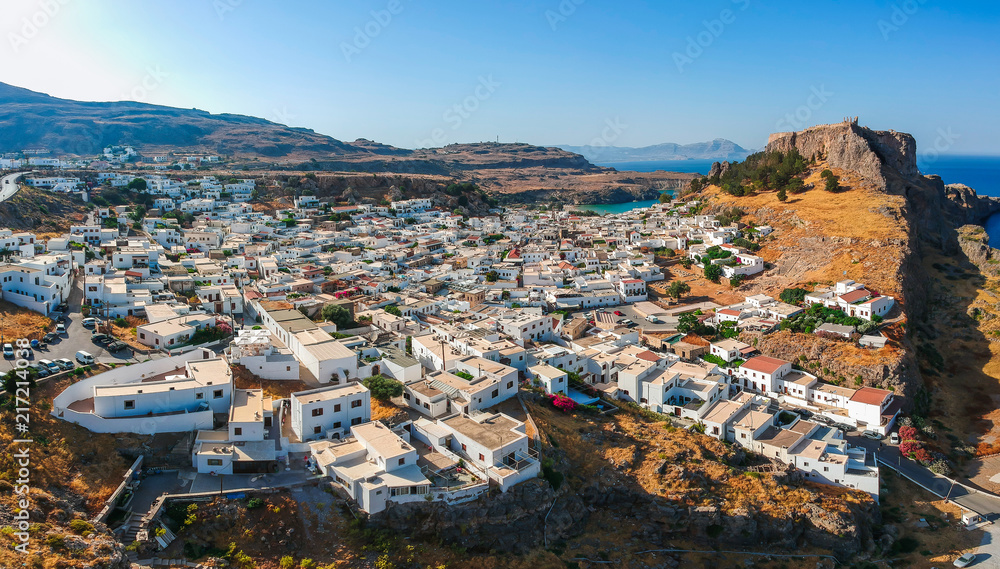 Naklejka premium Aerial birds eye view drone photo of village Lindos, Rhodes island, Dodecanese, Greece. Sunset panorama with castle, Mediterranean sea coast. Famous tourist destination in South Europe.