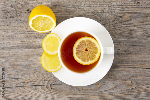Tea with lemon in a white mug on a wooden table. Top view. Copy space.