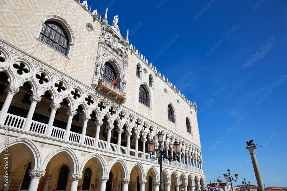 Venice, white Doge palace facade and San Marco lion statue on column in a sunny day, clear blue sky in Italy