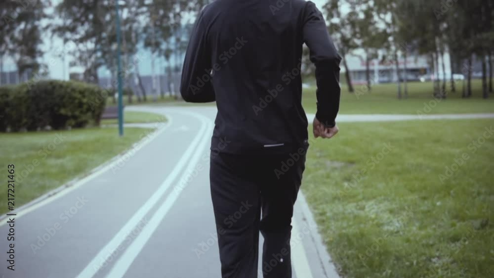 Man running along a city park road. Slow motion. Back view. Tilt up. Successful businessman jogging on a green alley. Man running along a city park road. Slow motion. Back view. Tilt up. Successful businessman jogging on a green alley.