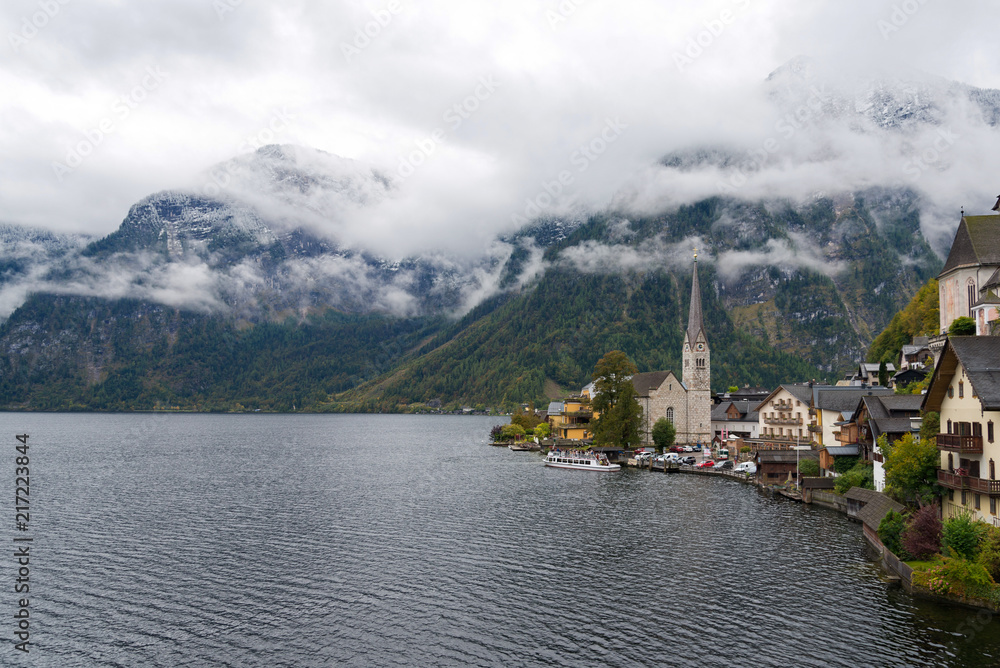 Scenry of lake Hallstatt, Austria  surrounded by hallstatt village, church and range of Alp during gloomy, foggy and cloudy sky. 