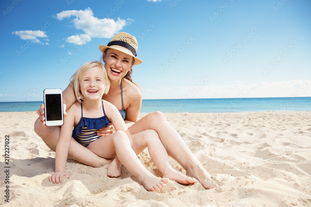 mother and child on seashore showing cellphone blank screen