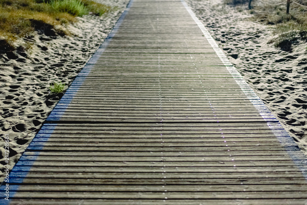 Obraz premium Wooden path to reach the beach on the lit sand at night.