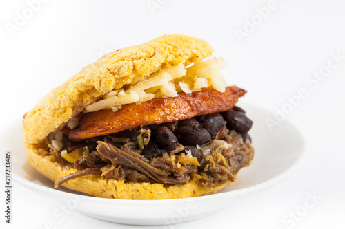 Arepas filled with shredded beef, black beans, plantain and cheese served in a white dish on white background