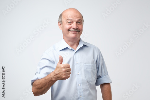 Obraz na plátně Handsome, bald man with his thumb up in sign of optimism on white background
