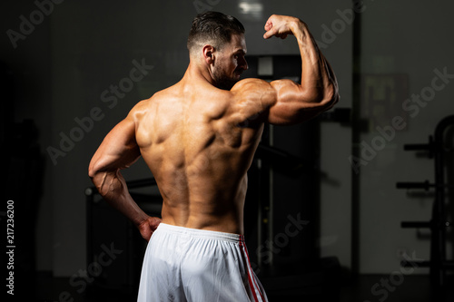 Biceps Pose Of A Young Man In Gym