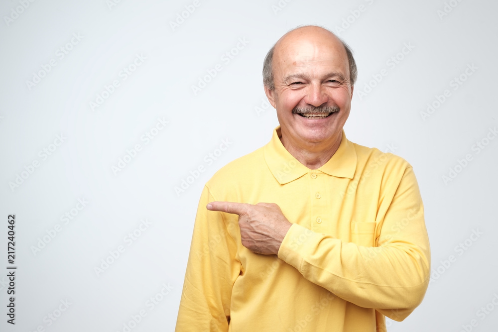 Happy senior man in yellow tshirt looking at camera, smiling and pointing aside with hand. Happy senior man in yellow tshirt looking at camera, smiling and pointing aside with hand.
