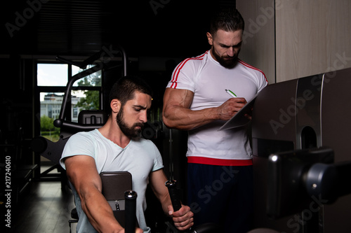 Man Train Back On Machine With Personal Trainer