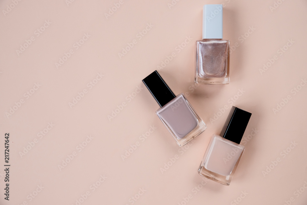 © Yulia - Creative flat lay of fashion bright nail polishes on a beige background. Minimal style. Copy space. Beauty blogger concept. Top view. Nude tones.