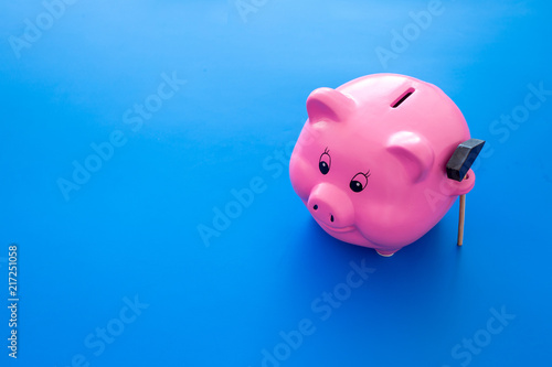 Piggy bank. Moneybox in shape of pig near hammer on blue background copy space
