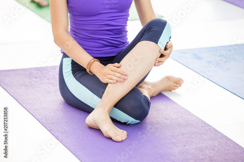 Young sporty woman practicing yoga at class, doing stretching exercise. Close-up detail view of leg and hand photo