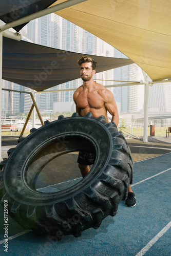 Young arab sports man exercising with truck tyre outdoors in Dubai during summer time.