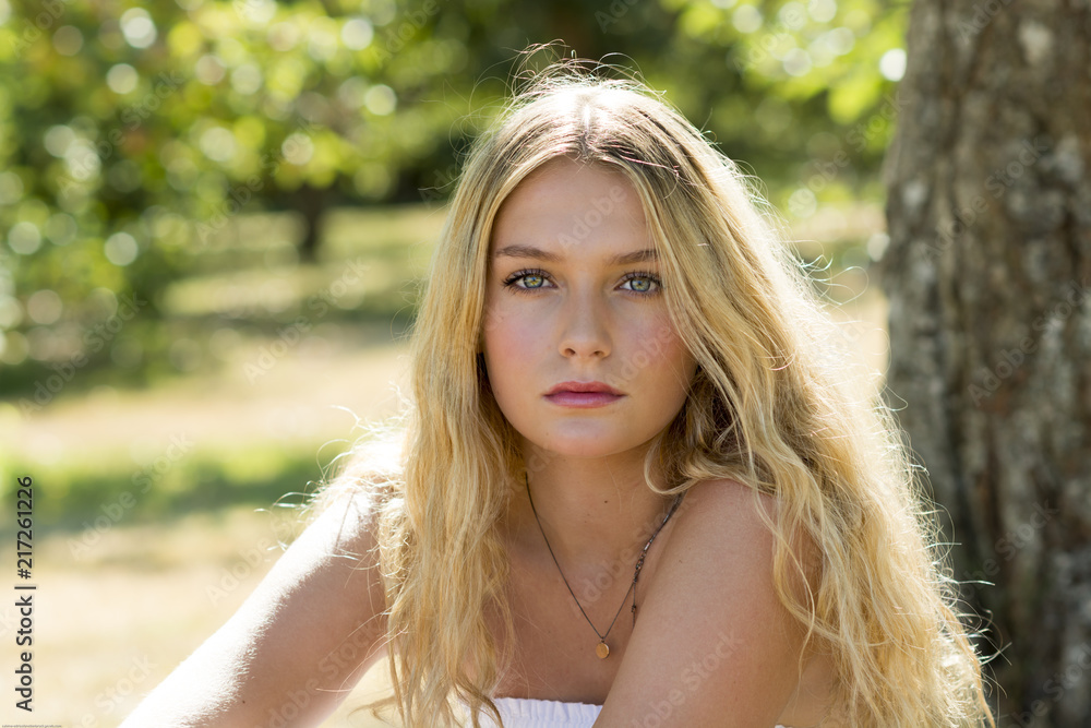Naklejka premium Portrait of young woman with long blonde hair in a park in sunshine