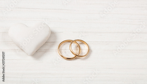 Close up view of golden wedding rings and a white heart, isolated, copy space, on a white wooden background.
