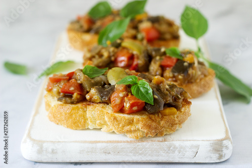 Bruschetta with caponata or ratatouille from various vegetables on a light background.