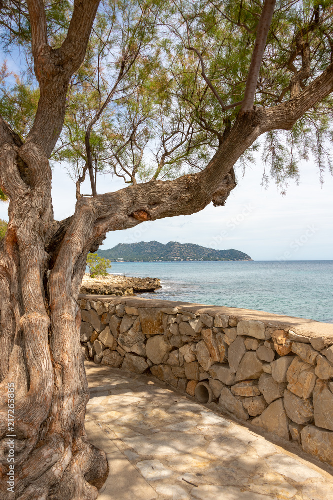 Natural stone wall on the promenade from the resort of Cala Millor with a view of the Mediterranean Sea and the hills on the Spanish Balearic island of Mallorca
