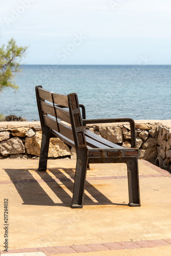 A bench on the seafront in the holiday resort Cala Millor with a beautiful view of Mittelmerr on the Spanish Balearic island Mallorca in front of a bright blue sky © PhotoArt Thomas Klee