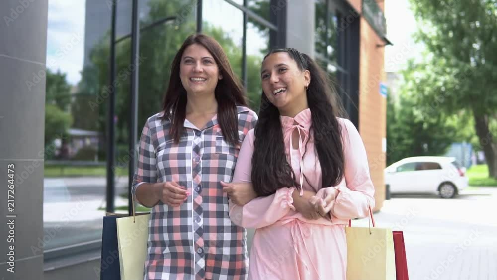 Two girls in beautiful dresses go after shopping near the shopping center holding packages with purchases having a good disposition. slow motion. HD Two girls in beautiful dresses go after shopping near the shopping center holding packages with purchases having a good disposition. slow motion. HD