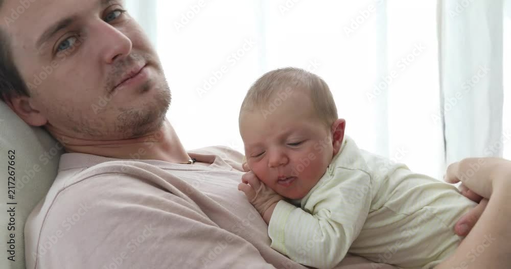 Side view of casual man sitting with charming little newborn baby on hands kissing in head Side view of casual man sitting with charming little newborn baby on hands kissing in head