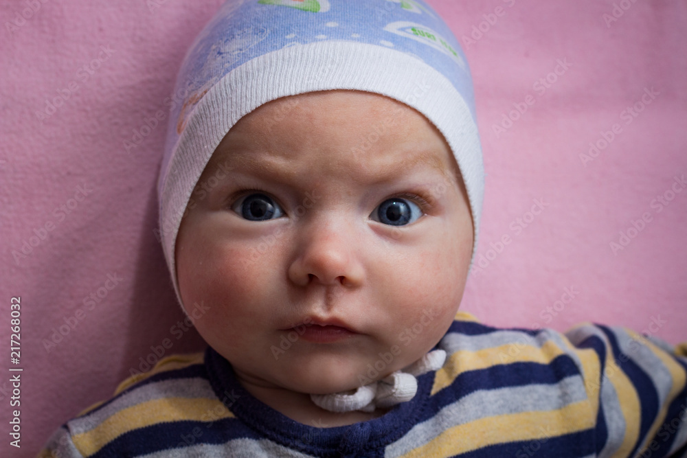 Little baby in clothes with a funny face on pink sheet. Flat lay Little baby in clothes with a funny face on pink sheet. Flat lay
