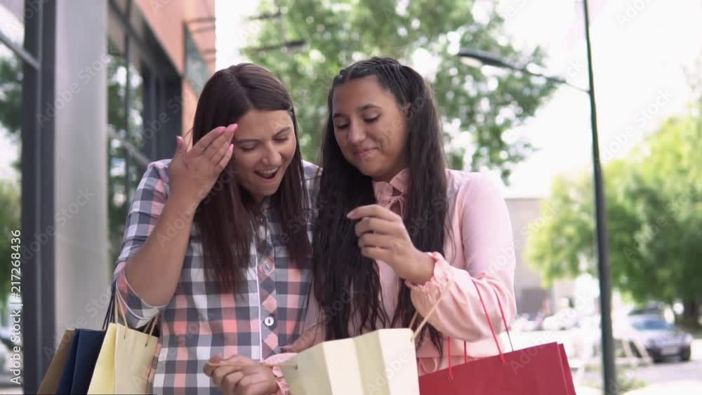 Two attractive girls in beautiful dresses go after shopping near the mall holding shopping bags. slow motion. HD Two attractive girls in beautiful dresses go after shopping near the mall holding shopping bags. slow motion. HD