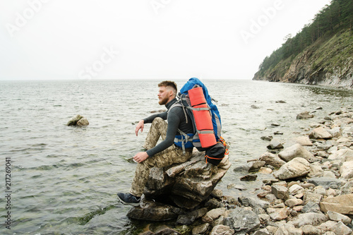 Young guy tourist with backpack on lake and mountains background