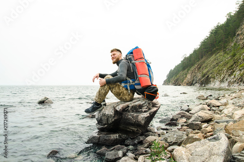 Young guy tourist with backpack on lake and mountains background