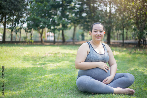 Asian pregnant woman was holding a glass of milk to drinking for a good health mom and baby with the green park background © Uraiwon