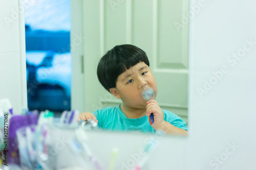 A boy brushes his teeth by himself in the restroom.