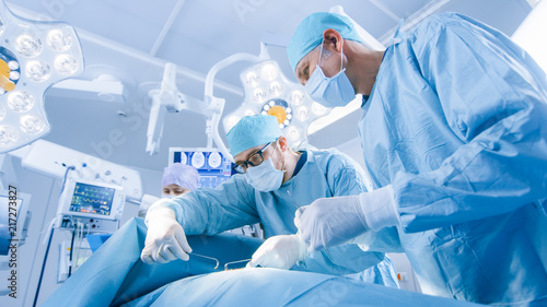 Low Angle Shot of a Diverse Team of Professional Surgeons Performing Invasive Surgery on a Patient in the Hospital Operating Room. Surgeons Use Instruments photo