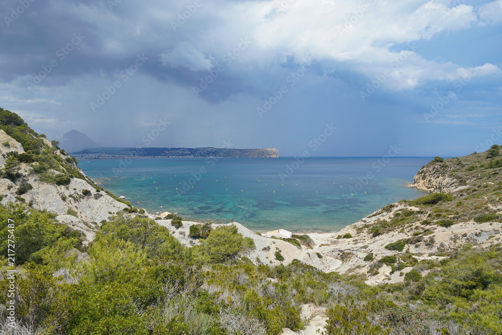 Spain Javea bay, Cala Sardinera with stormy sky and the cape San Antonio in background, Mediterranean sea, Costa Blanca, Alicante, Valencia