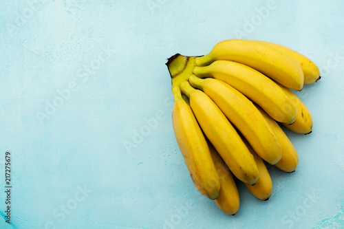 Branch of fresh baby bananas on turquoise concrete background. Natural tropical fruit. Top view.