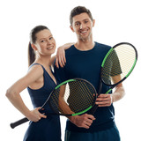 Couple of young tennis players on white. Woman leant on man's shoulder, both holding racquets and giving friendly smiles.