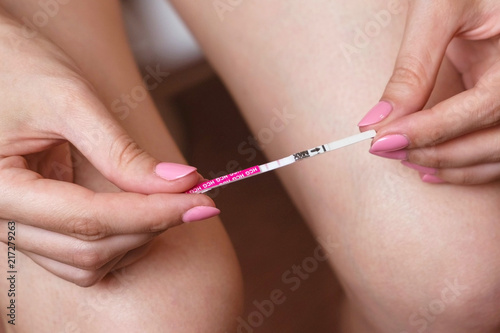 Woman makes a pregnancy test. Waiting for the result, looking at the test strip. Two stripes on test. Close-up hands and legs.